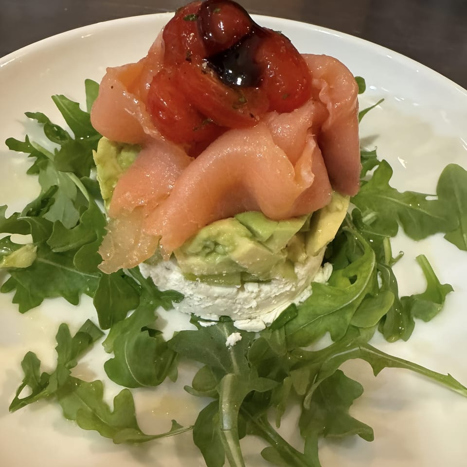 Italian appetizer with stacked ricotta, avocado, prosciutto, and roasted tomatoes on a bed of arugula.