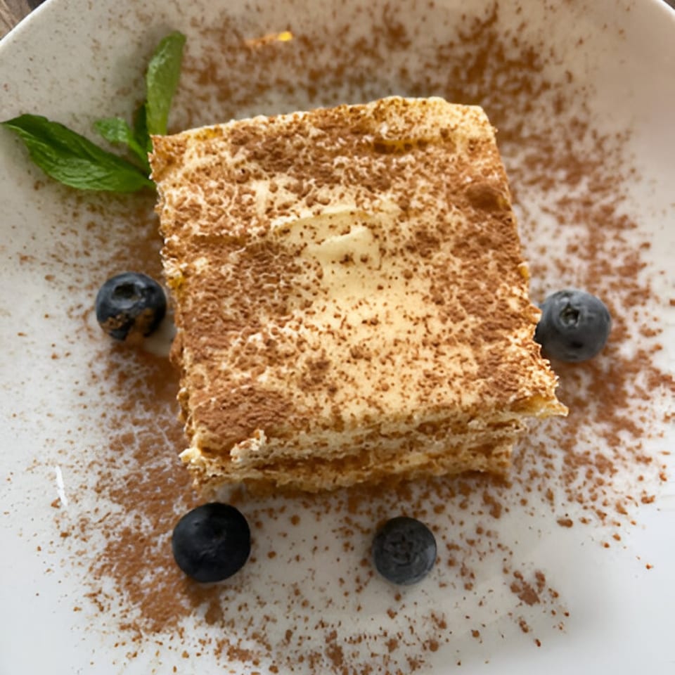 Tiramisu dessert with cocoa powder, blueberries, and mint on a white plate.