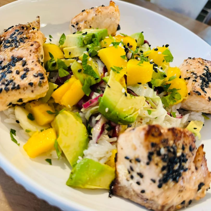 Grilled salmon with black sesame seeds, avocado, mango, and rice in a white bowl.