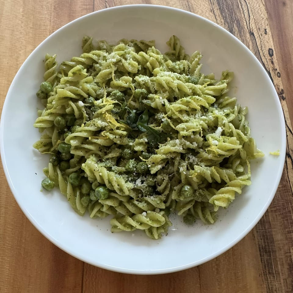 A white bowl filled with Mambo Italiano's green pesto fusilli pasta, peas, and grated cheese.