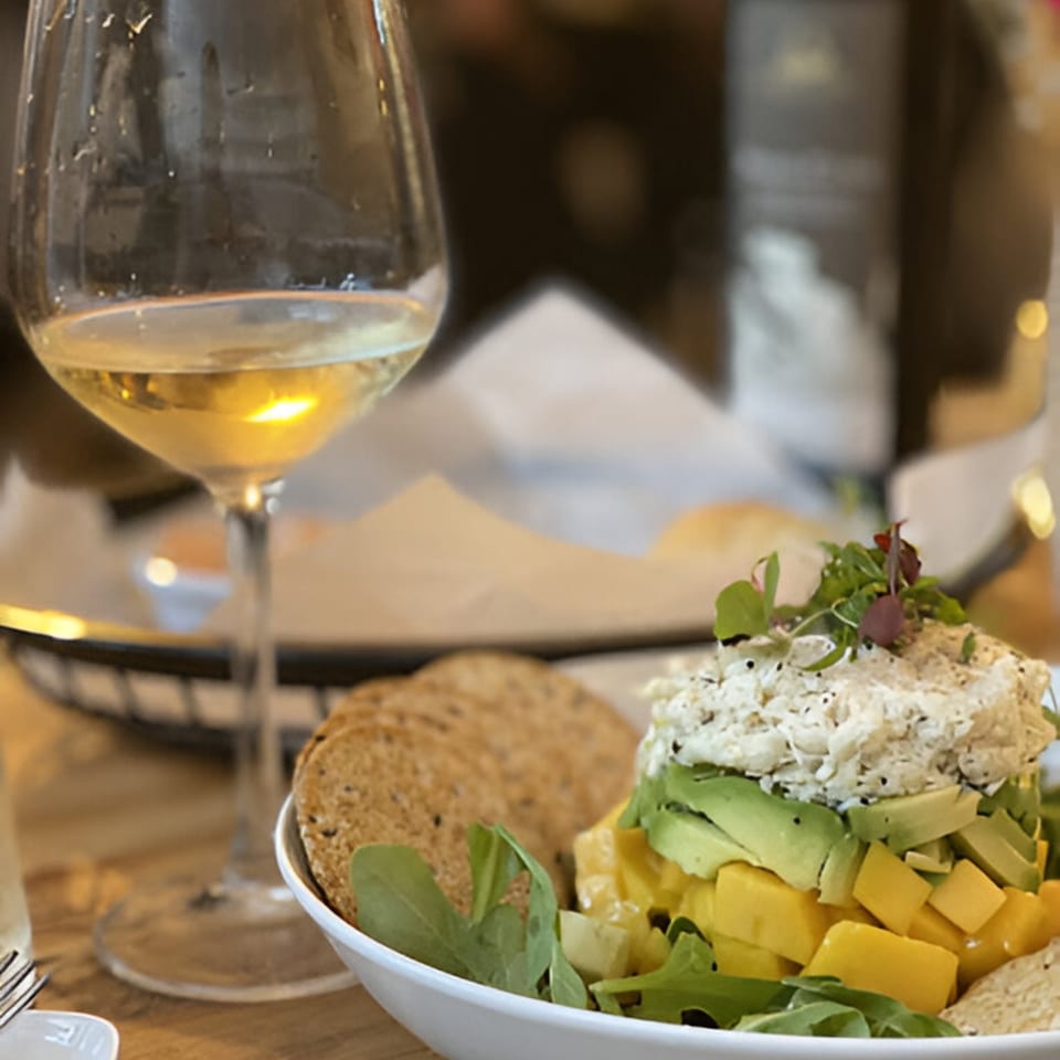A white wine glass next to a layered salad with crab, avocado, mango, and crackers.