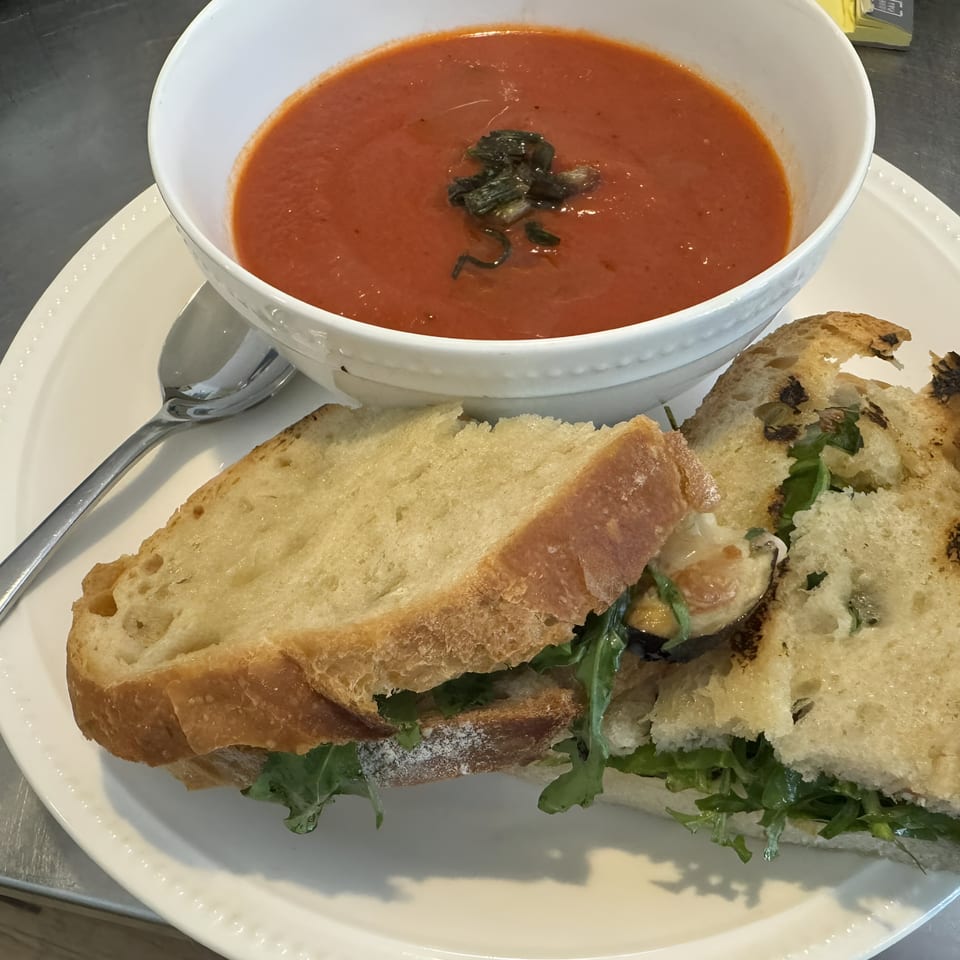 A bowl of Mambo Italiano's tomato soup with basil, alongside a sandwich on toasted bread.